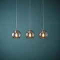 Three modern pendant lights with smoked glass globe shades and glowing bulbs hanging against a teal wall.