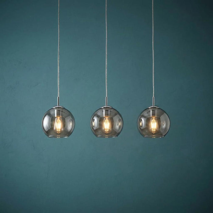 Three modern pendant lights with smoked glass globe shades and glowing bulbs hanging against a teal wall.