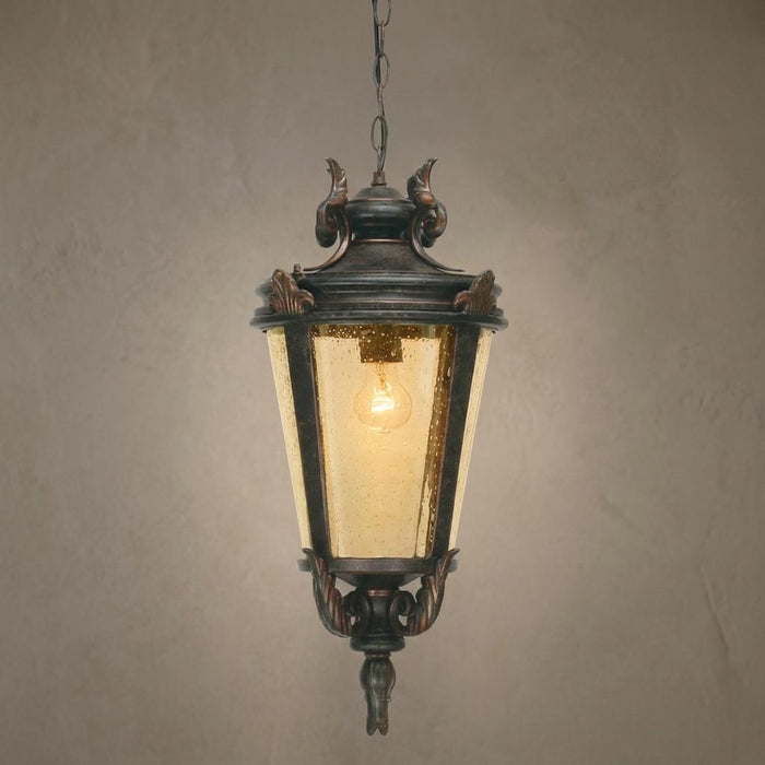 Ornate weathered bronze outdoor pendant light with amber seeded glass hanging against a textured wall.