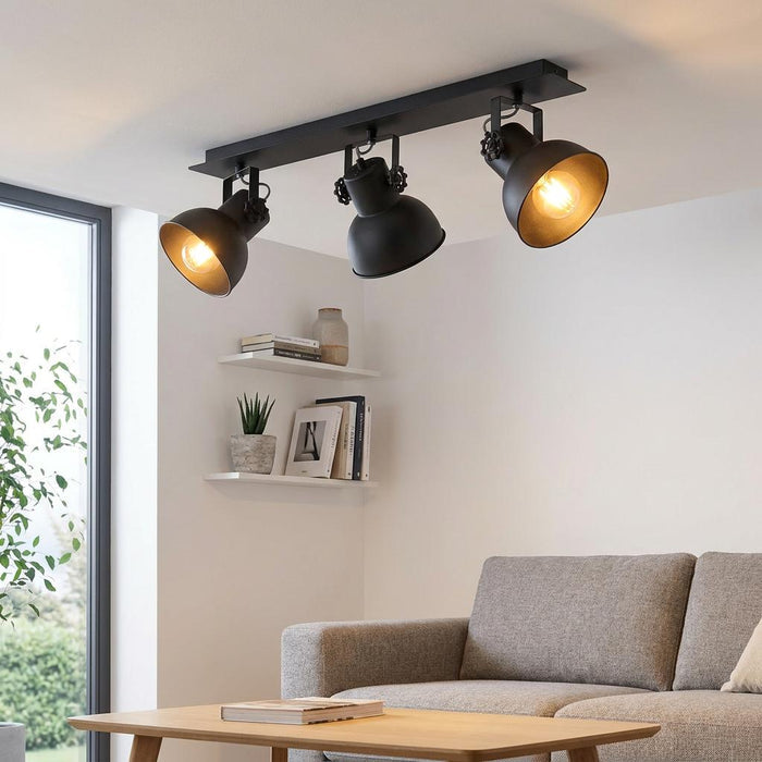 Eglo Barnstaple 1 black 3-light bar spotlight on a ceiling, illuminating a modern living room with a grey sofa.
