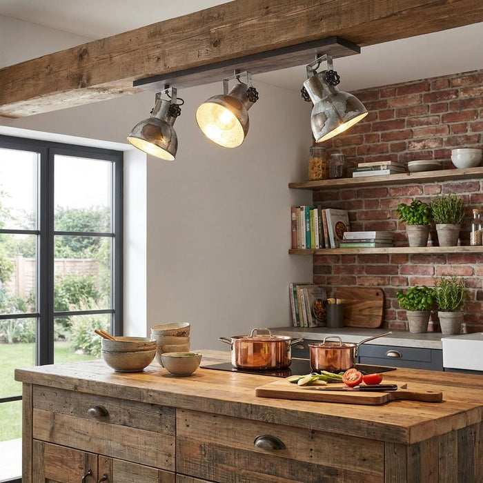 Three distressed steel spotlights on a dark wood bar, mounted to a ceiling beam above a rustic kitchen island.