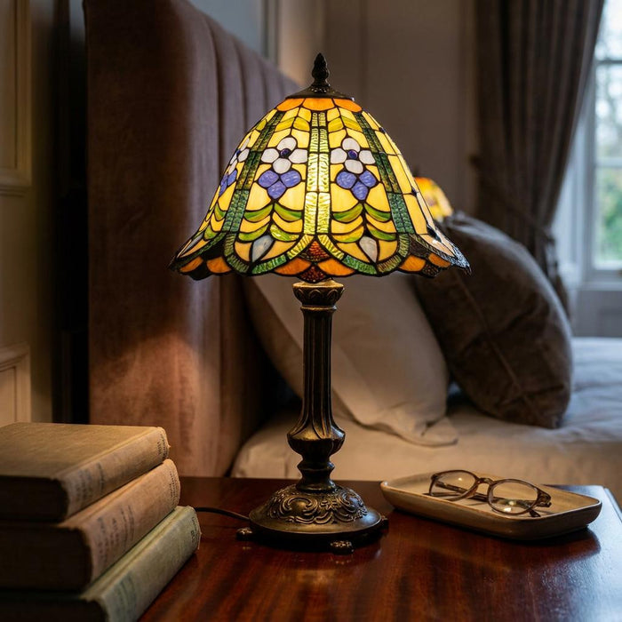 Floral Tiffany table lamp with a stained glass shade glowing on a wooden bedside table next to books.