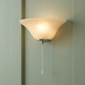 A wall-mounted champagne alabaster glass half coolie light with a pull cord, glowing against a green paneled wall.