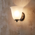 Bell-shaped frosted alabaster glass wall light with a cord pull, mounted on a textured rustic wall.