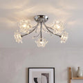 Five-light chrome semi-flush ceiling fixture with glass flower shades glowing in a modern room.
