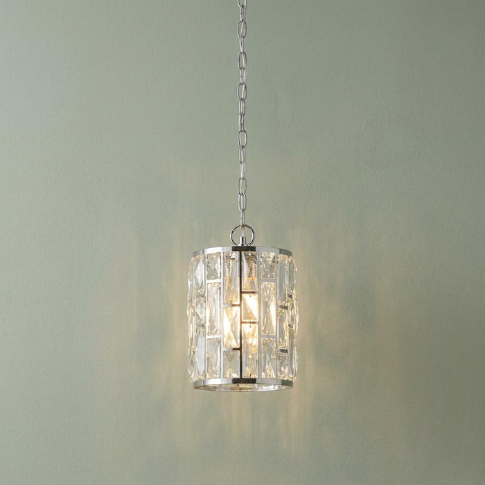 Bijou 1 light chrome pendant with a cylindrical crystal glass shade hanging from a chain against a pale wall.