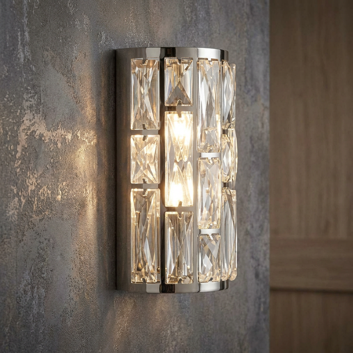 Modern chrome wall light with rectangular crystal accents glowing warmly on a textured gray wall.