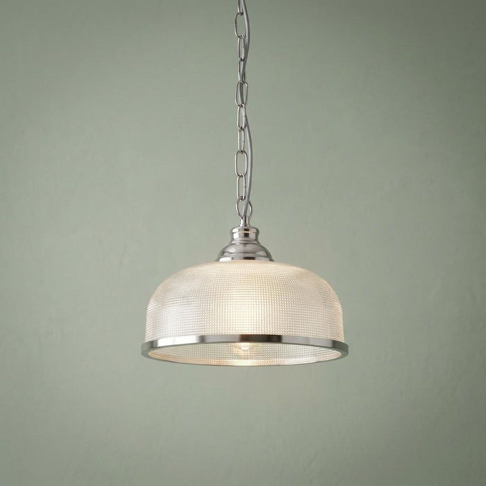 Silver pendant light with a ribbed holophane glass dome shade hanging against a sage green background.