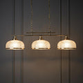 Three-light brass bar pendant with holophane glass shades suspended against a dark paneled wall.