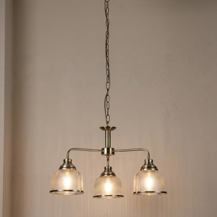 Bistro II 3-light brass pendant with ribbed glass shades suspended from a chain against a plain wall.