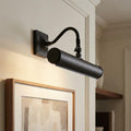Matte black picture light with a cylindrical head and curved arm illuminating a framed artwork on a white wall.