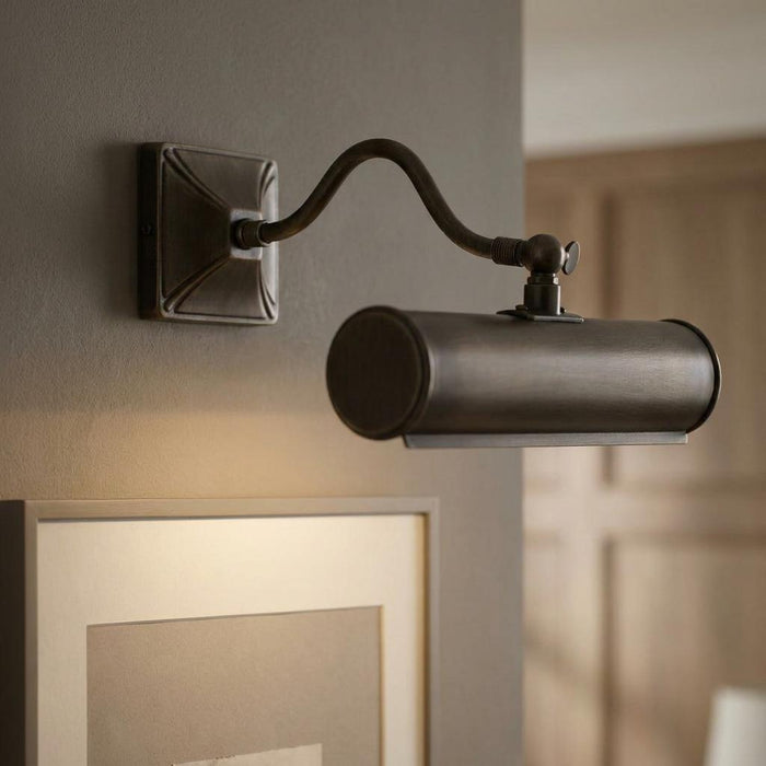 Traditional dark bronze picture light with a curved arm mounted on a grey wall above a framed picture.
