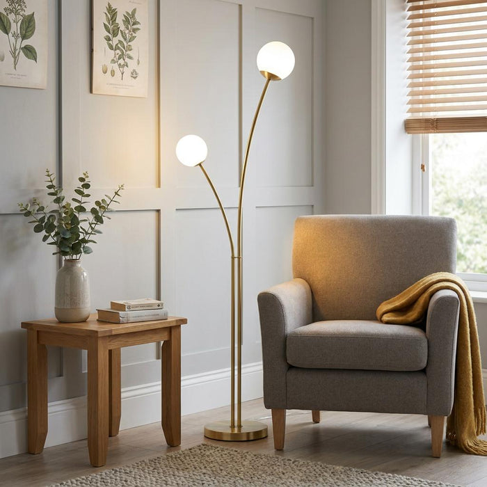 A modern brass floor lamp with twin globe shades illuminates a cozy living room next to a grey armchair.