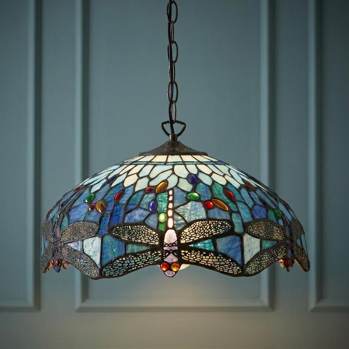 A blue dragonfly Tiffany ceiling pendant with stained glass and colorful beads, hanging against a blue paneled wall.
