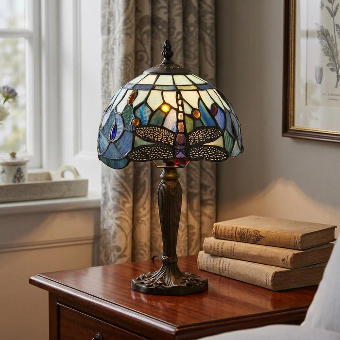 Blue Dragonfly Tiffany table lamp with a stained glass shade on a wooden table beside a stack of vintage books.