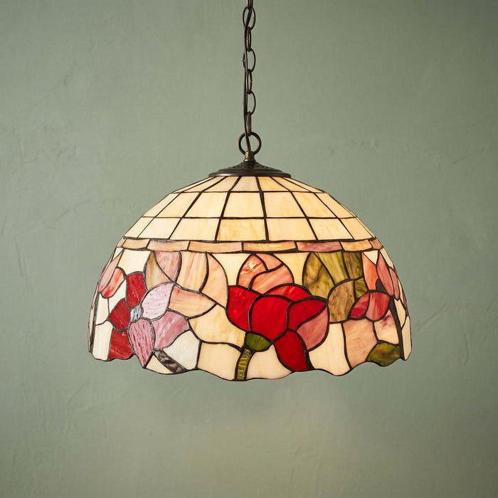Tiffany-style pendant light featuring a floral stained glass shade in red and cream, hanging against a green wall.