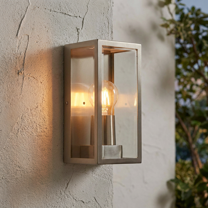 Illuminated Breton stainless steel rectangular wall lantern with glass panels on a textured exterior wall.