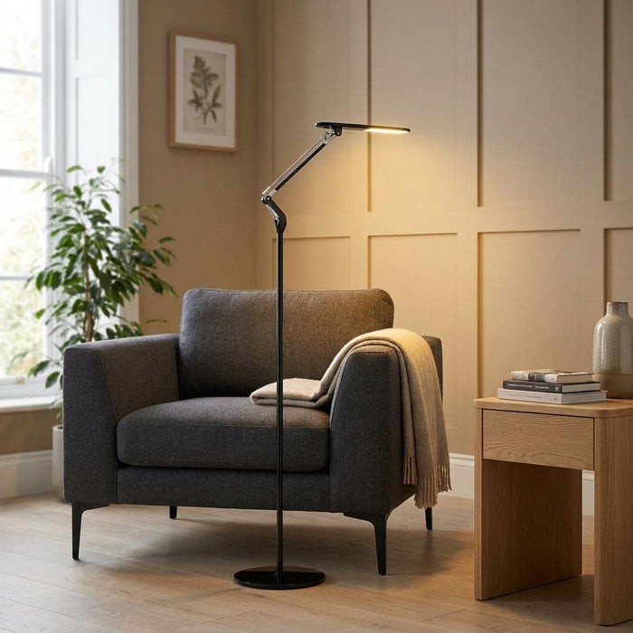 Slim black LED floor lamp with an adjustable neck illuminates a grey armchair in a contemporary living room.