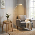 A white modern LED floor lamp illuminates a grey armchair in a cosy living room setting.
