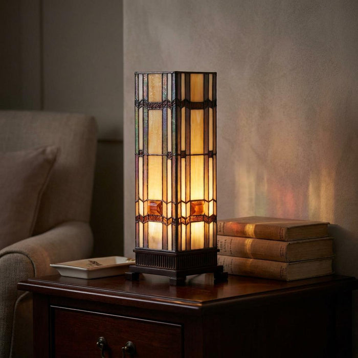 A square Tiffany-style table lamp with geometric stained glass on a wooden side table next to vintage books.