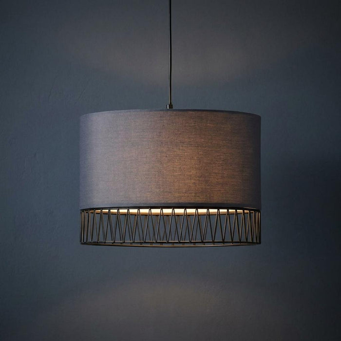 Burbank black pendant lamp with a grey fabric shade and wire cage bottom illuminated against a dark blue wall.