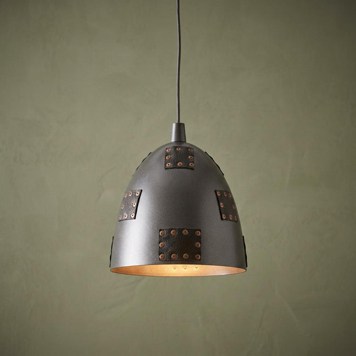 Grey metal dome pendant light with riveted leather patches hanging against a textured green wall.
