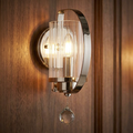 Cassie 1 light wall lamp in polished nickel with a ribbed glass shade and crystal drop on a wooden wall.