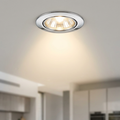 Illuminated polished chrome recessed downlight mounted in a white ceiling, casting a warm glow.