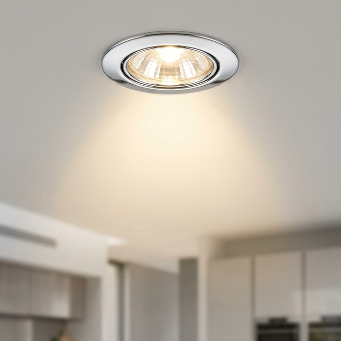 Illuminated polished chrome recessed downlight mounted in a white ceiling, casting a warm glow.