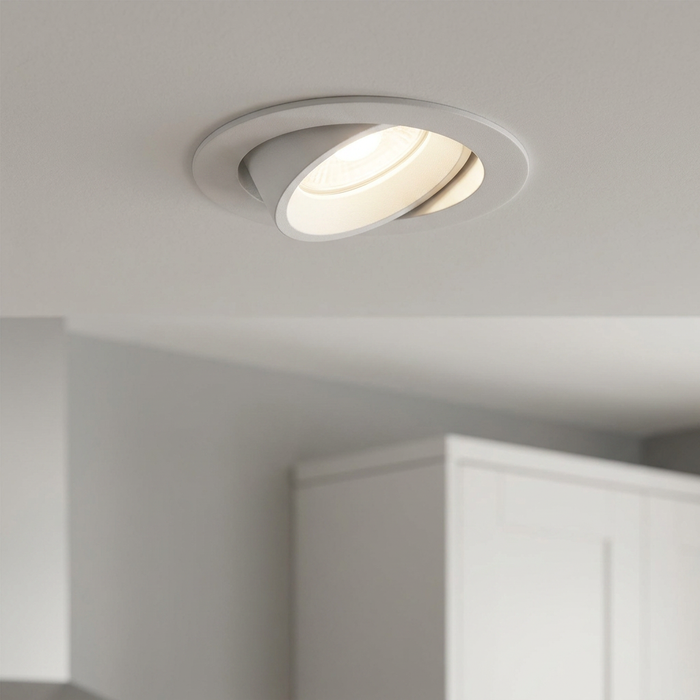 Cast matt white tilt recessed downlight glowing with warm light on a white ceiling.