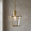 Polished brass lantern pendant with clear glass panels hanging against a textured grey wall.