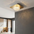 Square gold ceiling light with faceted acrylic dome casting glowing patterns in a modern kitchen.
