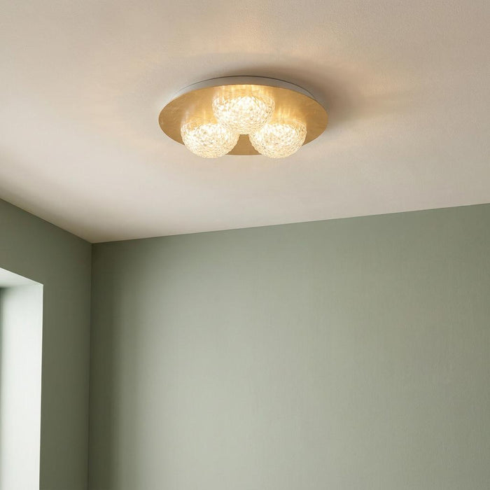 Gold flush ceiling light with three glowing textured acrylic globes, mounted in a room with light green walls.