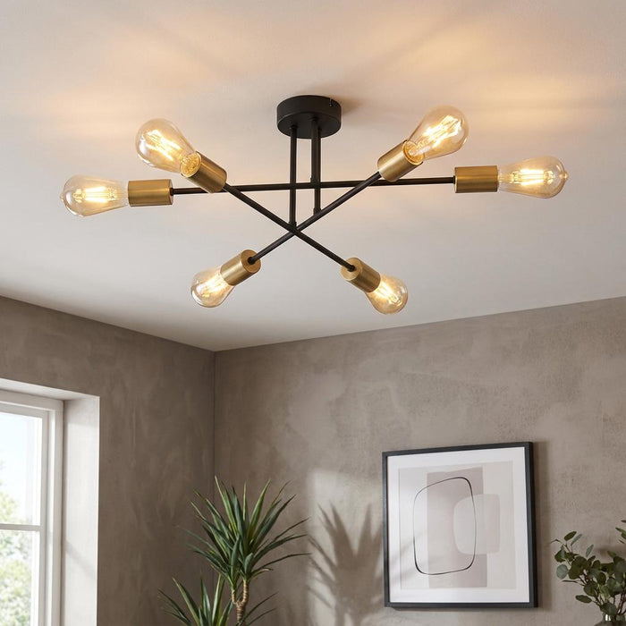 Chanin 6-light black and gold ceiling fixture with exposed bulbs in a modern room with a grey wall and artwork.