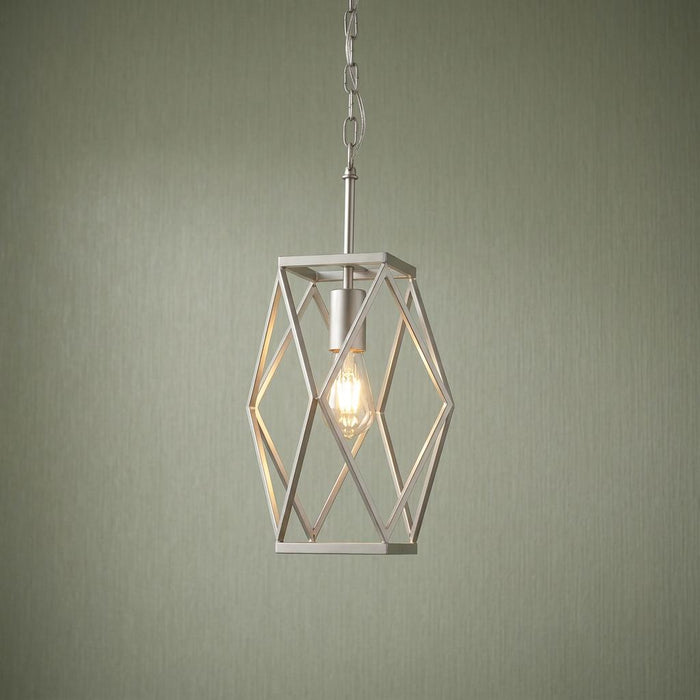 A satin silver geometric cage pendant light with an exposed glowing bulb against a green textured wall.