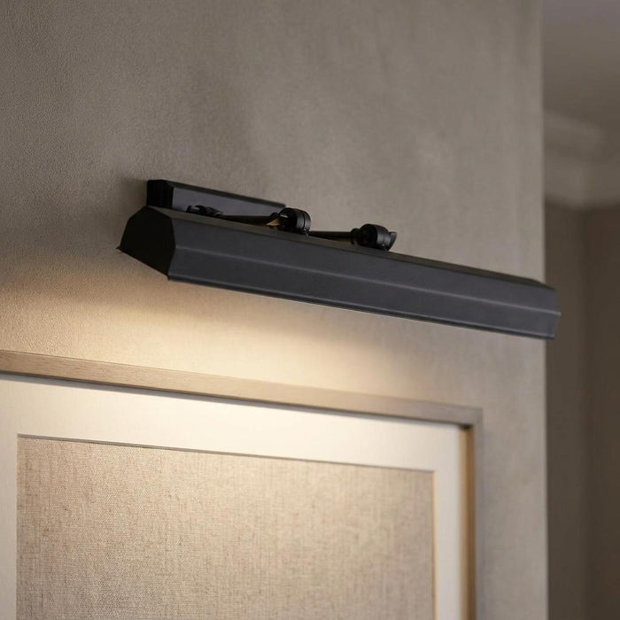 Black Chawton picture light mounted on a grey wall, illuminating a framed artwork below.
