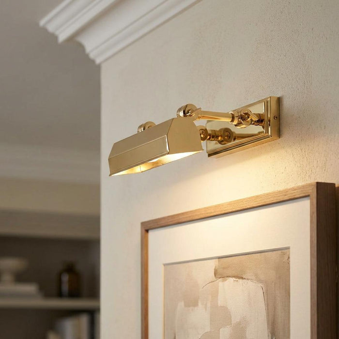 Polished brass Chawton picture light mounted on a wall above a framed artwork, casting a warm downward glow.