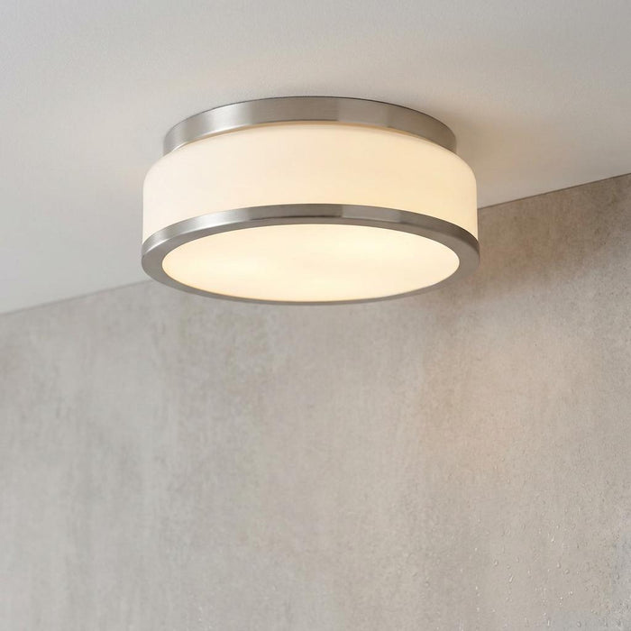 Satin silver bathroom flush ceiling light with an opal white glass shade, glowing against a white ceiling.