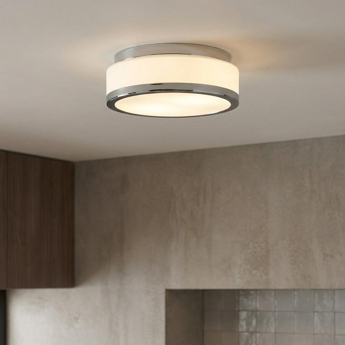 Modern circular flush ceiling light with chrome trim and white glass shade illuminated on a white ceiling.