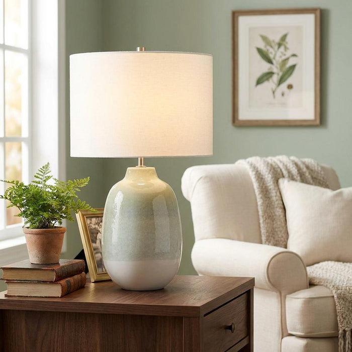 Chelsfield green and white ombre ceramic table lamp with a white drum shade lit on a wooden side table.