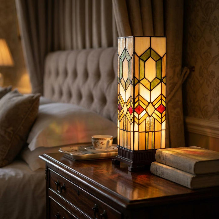 Geometric Tiffany-style square table lamp glowing on a wooden bedside table in a cozy bedroom setting.