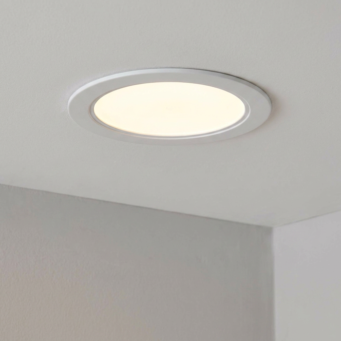 A white circular recessed ceiling light emitting a warm glow from a frosted diffuser.