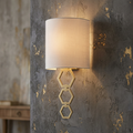 Aged brass wall light with three hexagonal rings and a white shade on a textured grey wall with gold accents.