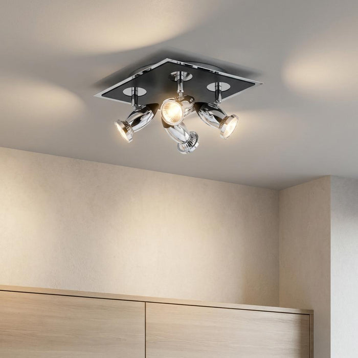 Chrome four-light square flush spotlight fixture illuminated on a ceiling above a wooden cabinet.