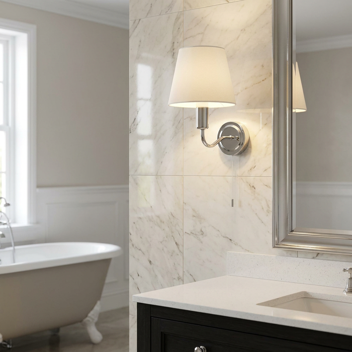 Chrome bathroom wall light with a white shade and pull cord on a marble wall next to a mirror.