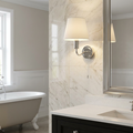 Chrome bathroom wall light with a white shade and pull cord on a marble wall next to a mirror.