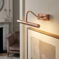 A copper LED picture light illuminating framed artwork on a wall in a contemporary living room setting.