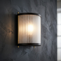 A Corona wall light with a bronze frame and ribbed glass emits a warm glow on a dark textured wall.