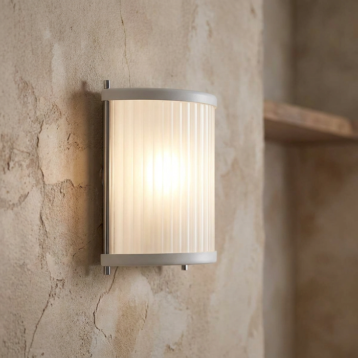 Modern curved wall light with ribbed glass and white trim, glowing on a rustic textured wall.