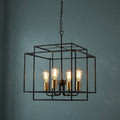 Geometric black frame pendant with four glowing bulbs and bronze lampholders against a dark teal wall.